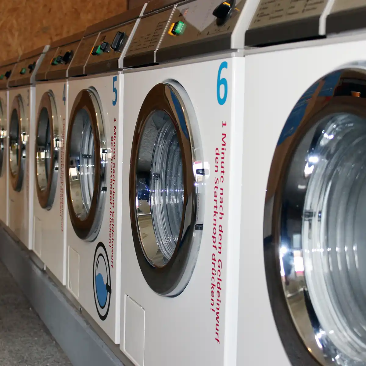 A row of washing machines, each with a large opening with chromed frames